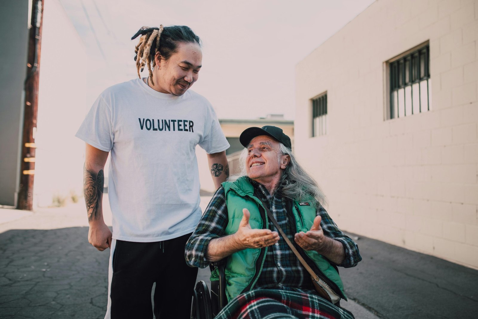 Smiling volunteer helping a senior man in a wheelchair outside on a sunny day.
